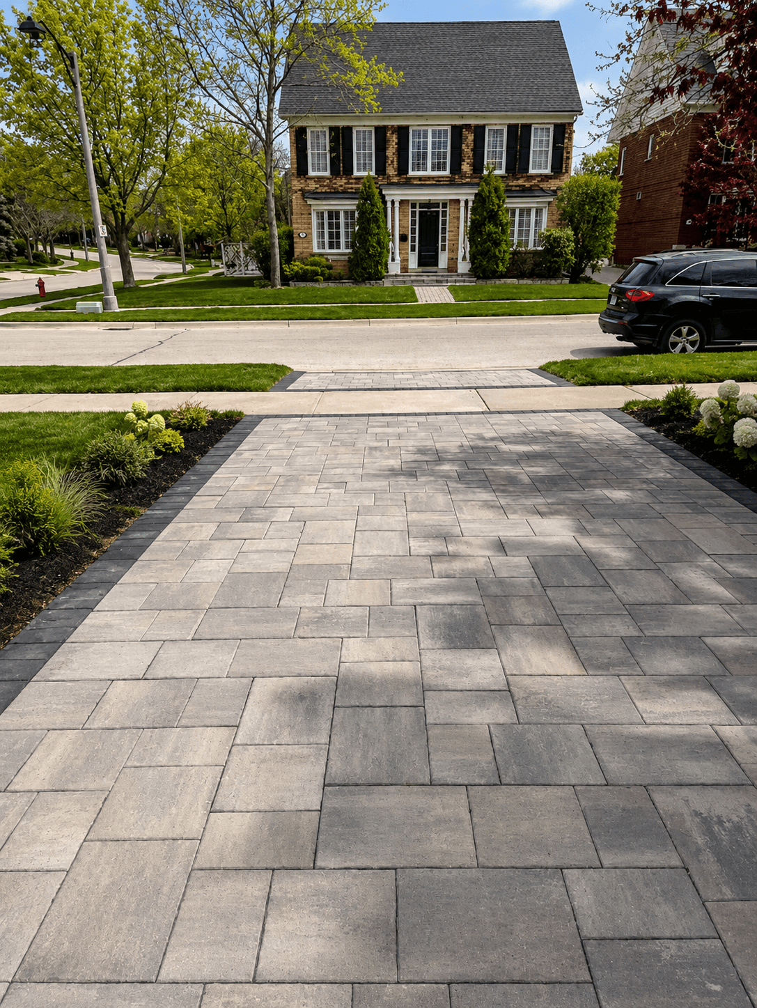 Wide interlocking paver driveway leading to a brick colonial home