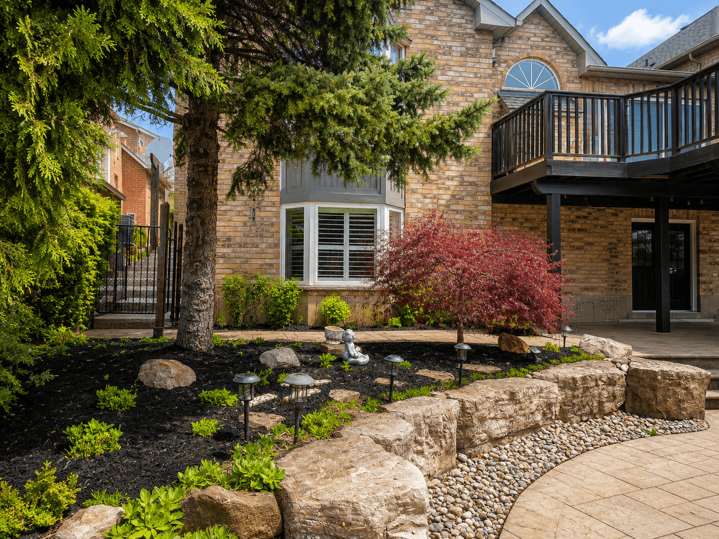 Armour stone landscape feature with river rock and Japanese maple